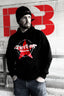 Male model wearing a black Dirtbag Clothing hoodie featuring a large red star graphic and bold Dirtbag logo, standing in a gritty urban concrete setting with a red DB graffiti style backdrop, showcasing alternative streetwear and casual outdoor apparel.