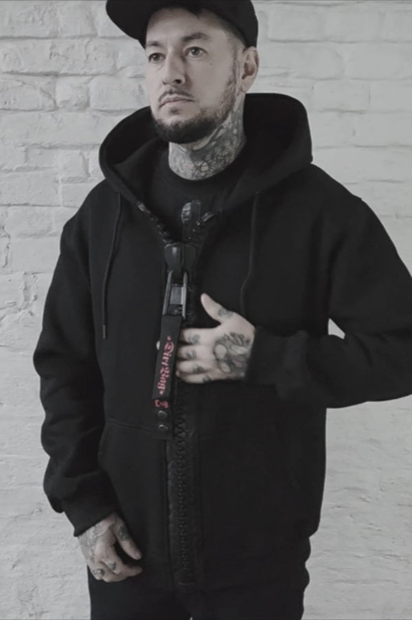 Dirtbag black men's T shirt with a bold vertical zipper graphic down the front, worn by a tattooed model standing against a white brick wall.